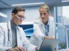 Two Doctors in Hospital Office Discuss a Diagnosis, Analyzing Data on a Laptop. Male and Female Medical Professionals Talking about Treatment, Drug Prescription during Telemedicine Call
